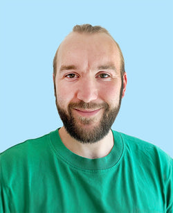Männliches Porträt mit blondem Haar Vollbart grünem T-Shirt hellblauem Hintergrund freundlichem Lächeln
