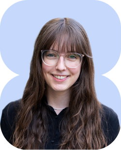 lächelnde junge Frau mit langen braunen Haaren und geradem Pony, filigrane Brille, schwarzes Hemd, pastellblauer Hintergrund