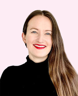 Fröhliche Frau mit langem braunem Haar schwarzem Rollkragenpullover und rotem Lippenstift vor pastellrosa Hintergrund