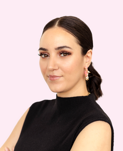 Frau mit zurückgebundenem dunkelbraunen Haar, dezentes Make-up, goldrosa Ohrring, schwarzer Rollkragenpullover, pastellrosa Hintergrund