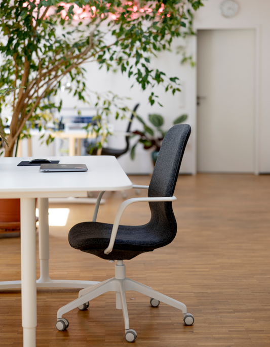 Schwarzer Bürostuhl auf Rollen vor weißem Tisch mit Laptop und Pflanze in hellem minimalistischen Büro