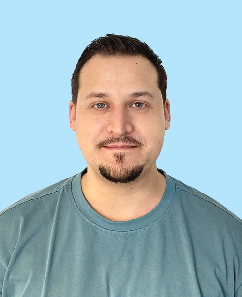 Mann mit dunklen Haaren und Ziegenbart blaugrünes Shirt hellblauer Hintergrund