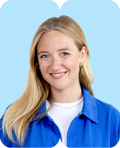 lächelnde junge blonde Frau mit blauer Jacke und Goldohrringen vor hellblauem Hintergrund