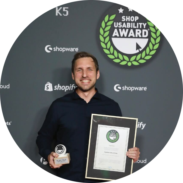 Strahlender Mann vor Sponsorenwand mit Shop Usability Award Logo hält Trophäe und Urkunde