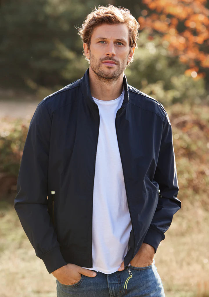 junger Mann in Jeans und dunkelblauer Jacke vor herbstlichem Laubwald, Hände in Taschen