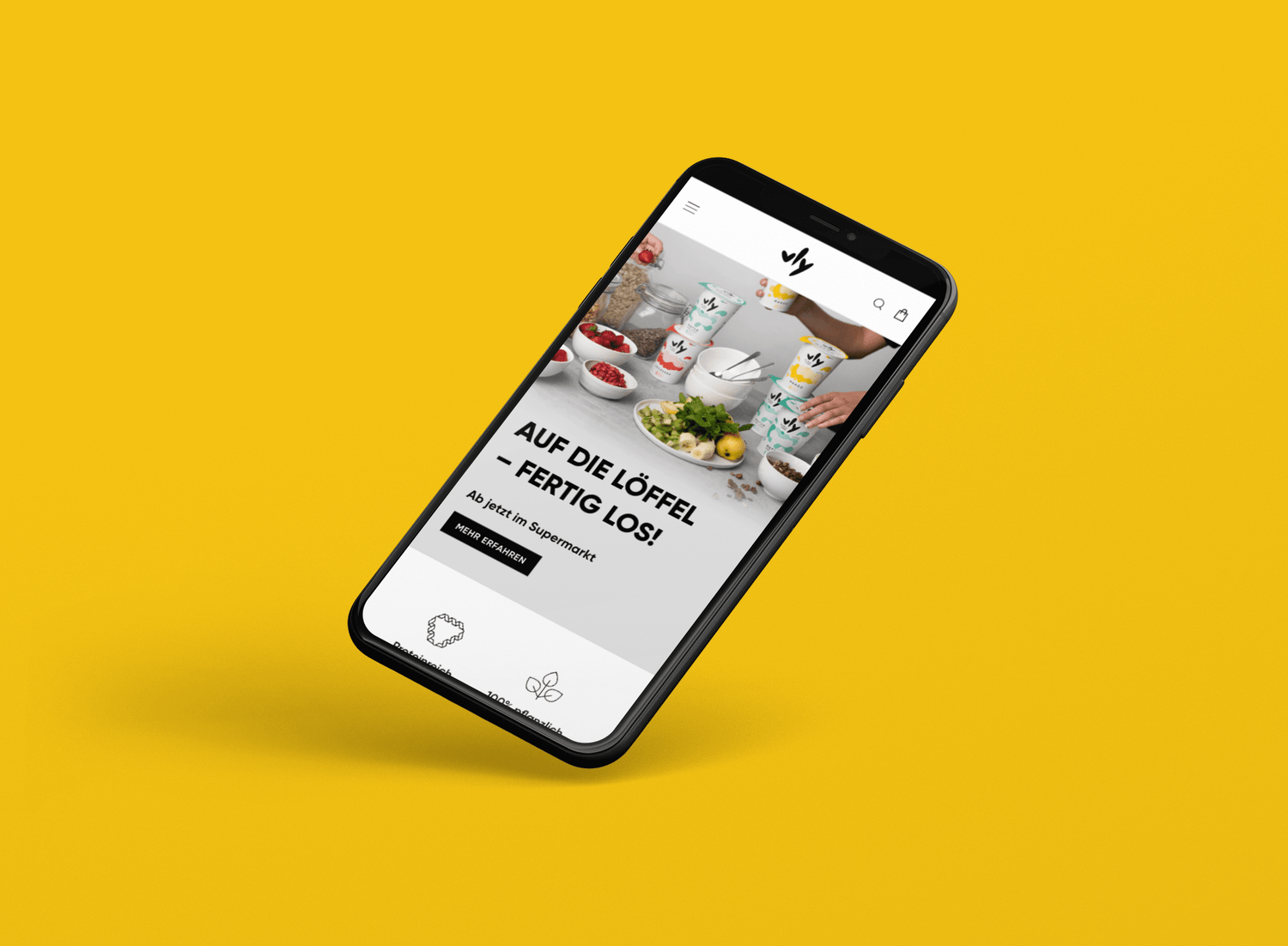 Schräg schwebendes Smartphone vor gelbem Hintergrund zeigt Webseite mit bunten Joghurtbechern, Schalen mit Erdbeeren und Bananenscheiben, Händen beim Anrichten