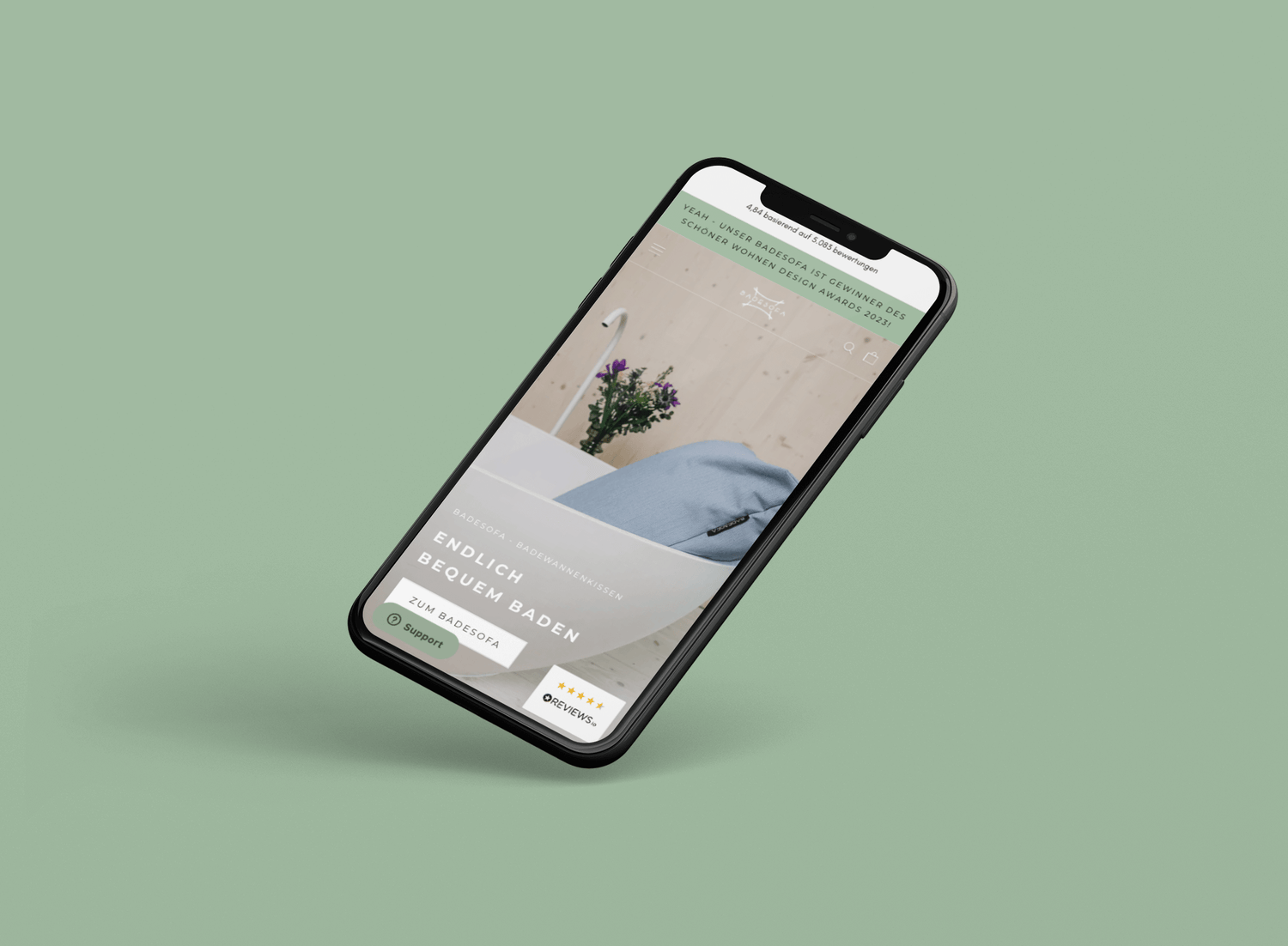 schwebendes Smartphone mit Website für blaues Badewannenkissen vor Blumenarrangement auf grünem Hintergrund