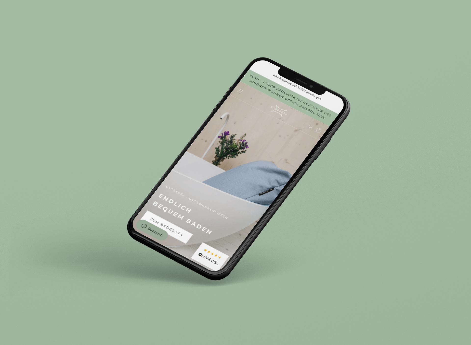 schwebendes Smartphone mit Website für blaues Badewannenkissen vor Blumenarrangement auf grünem Hintergrund