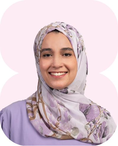 Lächelnde Frau mit floralem Hijab und pastellfarbenem Oberteil vor hellem Hintergrund