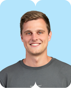Lächelnder junger Mann mit kurzem hellbraunem Haar und grauem T-Shirt vor hellblauem Hintergrund