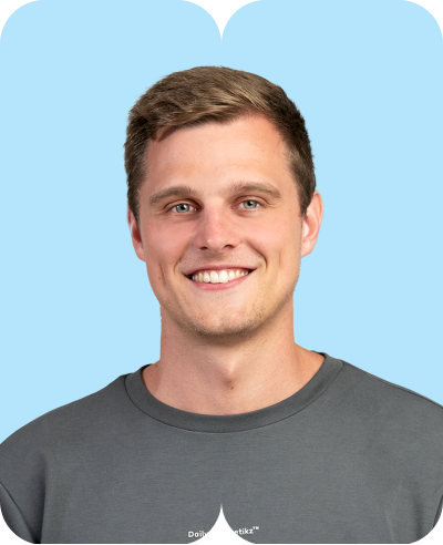 junger lächelnder Mann mit kurzem blondem Haar vor hellblauem Hintergrund in grauem T-Shirt