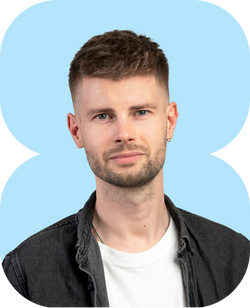 junger Mann mit kurzem Haarschnitt dezentem Bart weißem T-Shirt dunklem Hemd vor hellblauem abstraktem Hintergrund