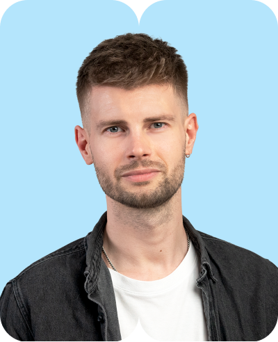 Junger Mann mit kurzem braunem Haar und Bart weißem T-Shirt schwarzer Jeansjacke vor hellblauem Hintergrund