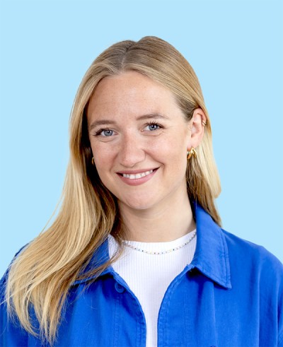 lächelnde Frau mit blonden Haaren und blauer Jacke vor hellblauem Hintergrund